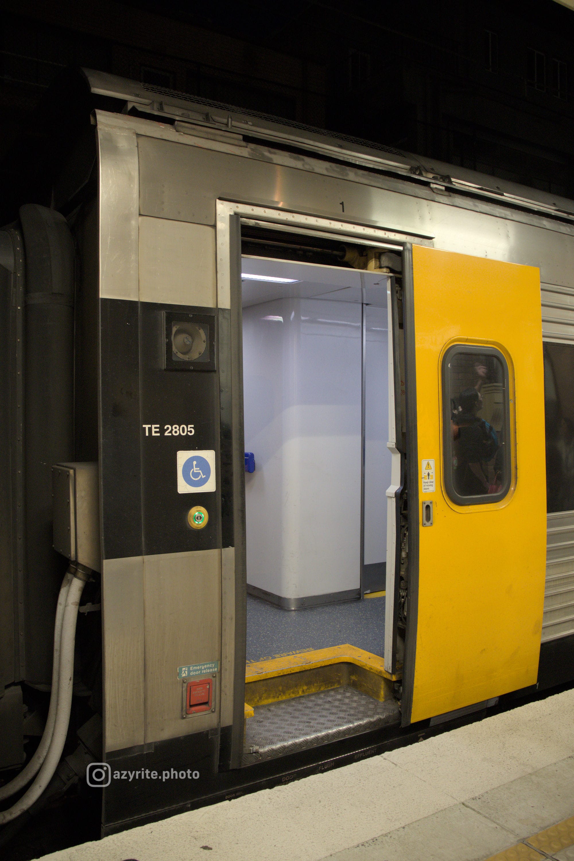 Portrait shot of the open yellow exterior door of an Endeavour railcar, revealing the brightly-lit white & grey interior 