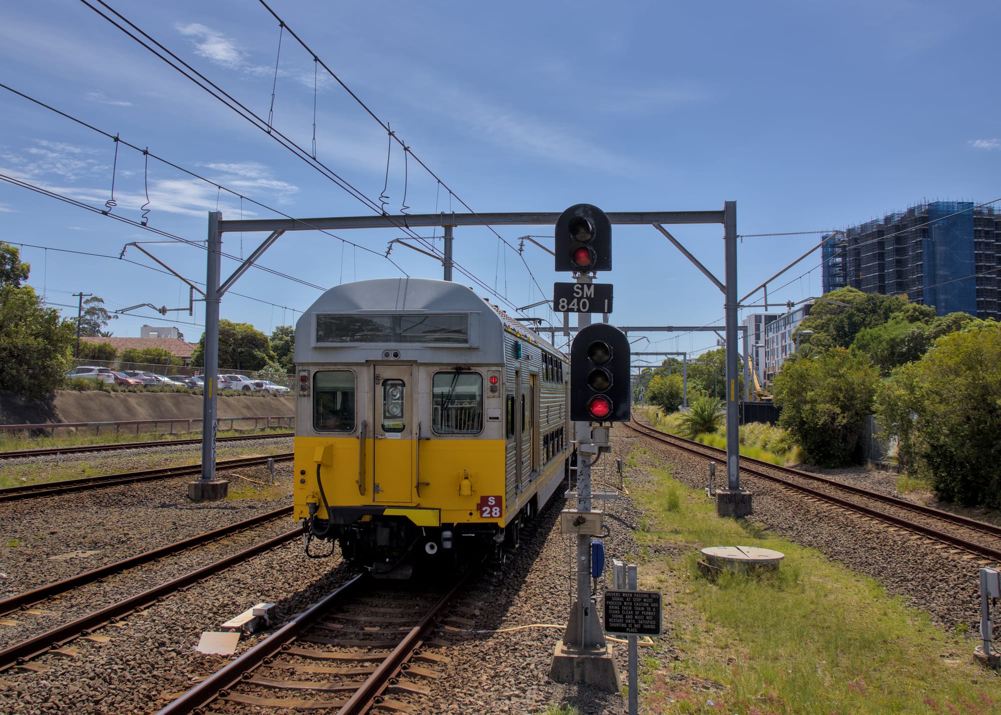 Rear of S28 passes signals, setting them to red on red, under overhead wiring and trackside greenery
