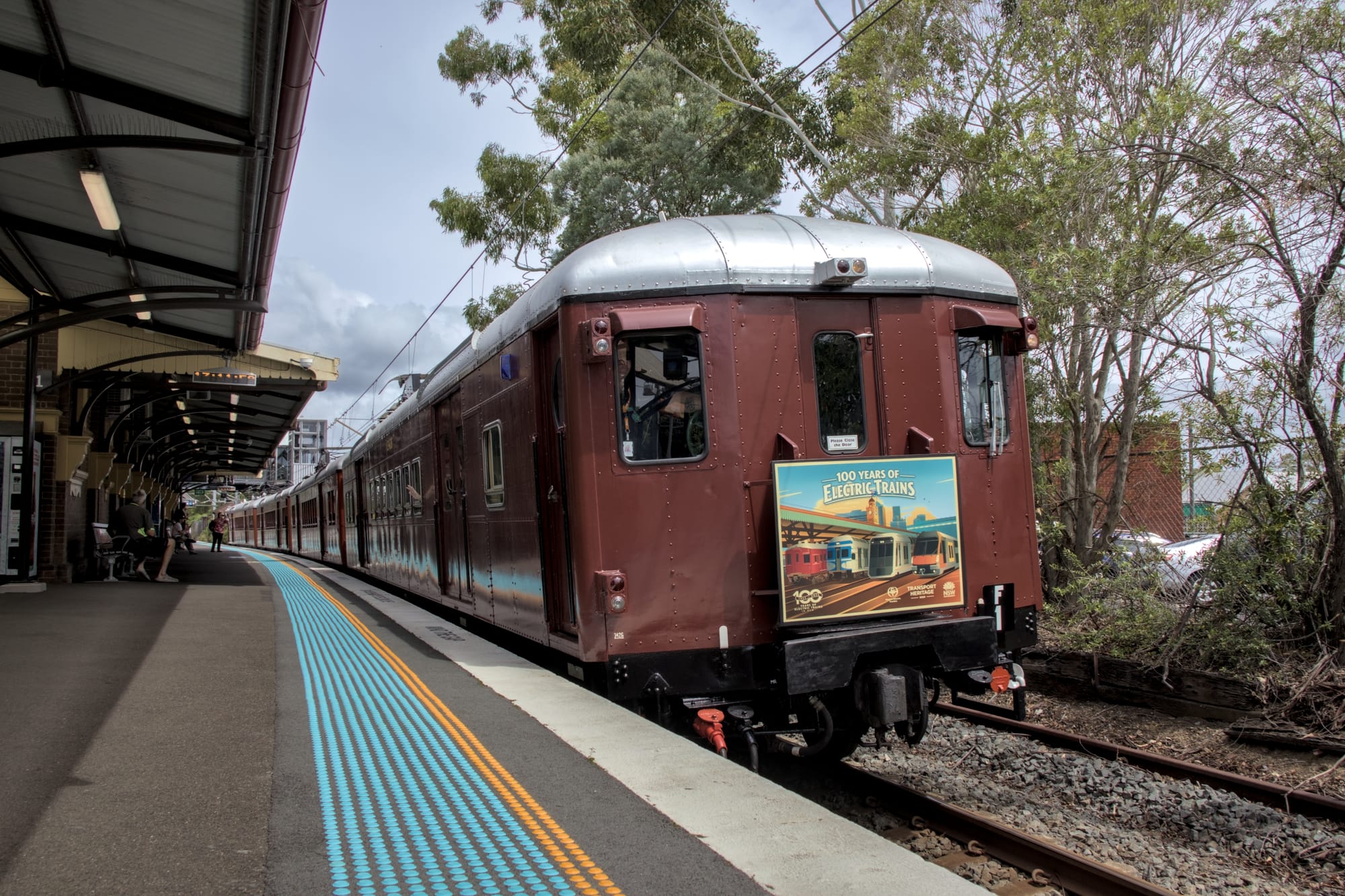 Low-angle shot of F1 curving as it passes Platform 1 at Mortdale, with some shrubbery visible on the far side