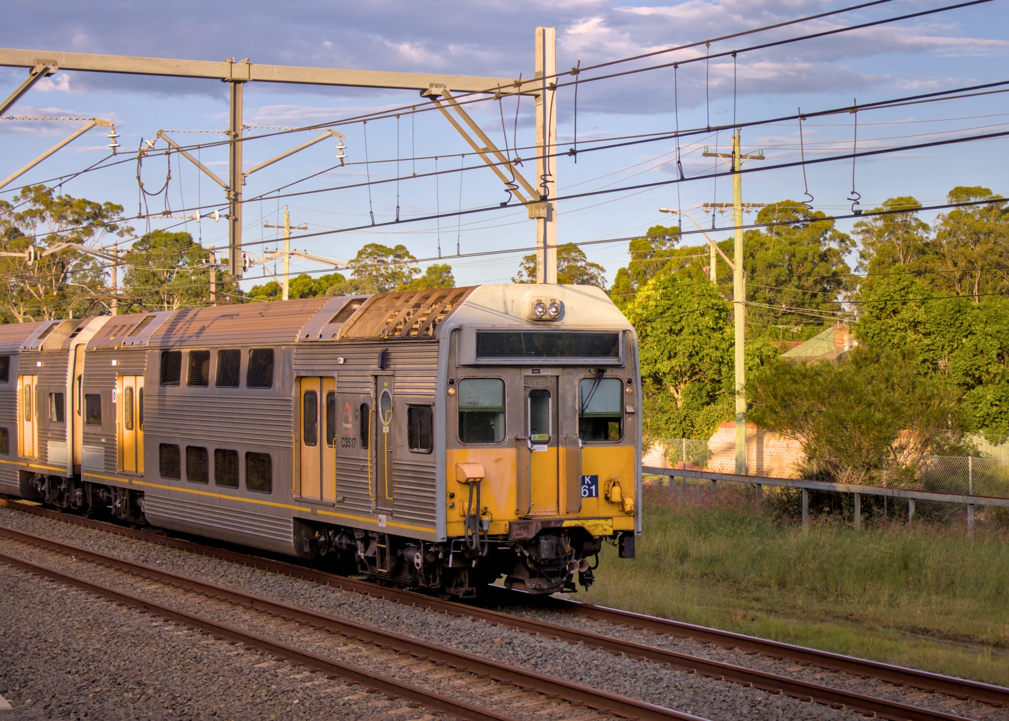 K Set travelling along tracks in the warm evening glow, with trees and dwellings in the background