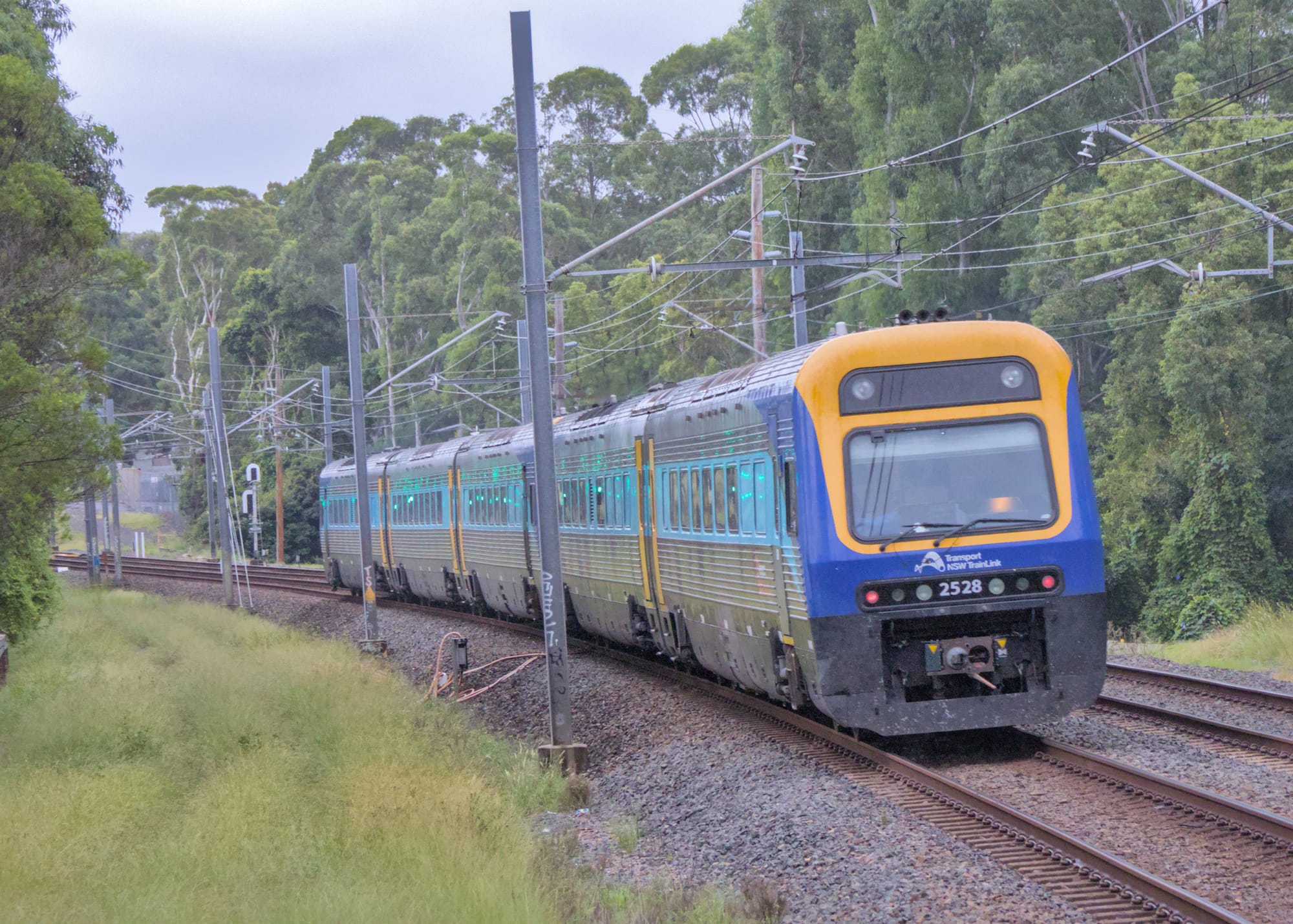 Blue and yellow accented silver-bodied diesel passenger train rounding a curve