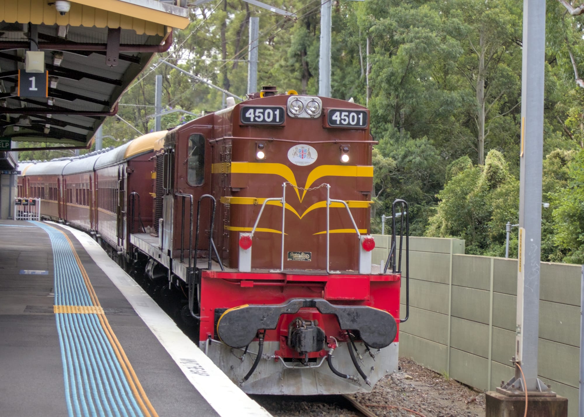 Maroon and red coloured vintage diesel locomotive leads around a curve through the platform
