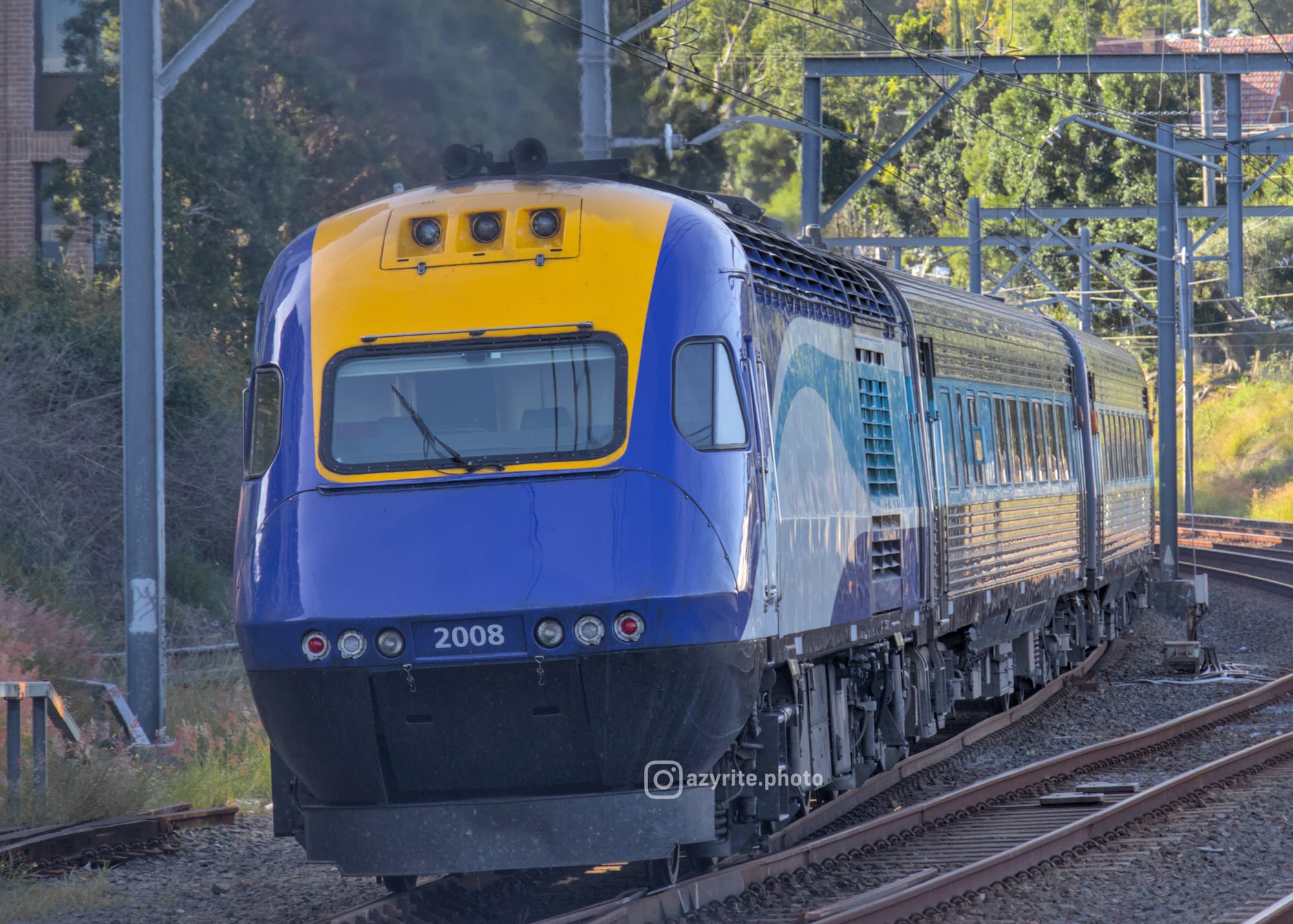 Blue and yellow XPT power car at the end of a consist of steel carriages going around a curve