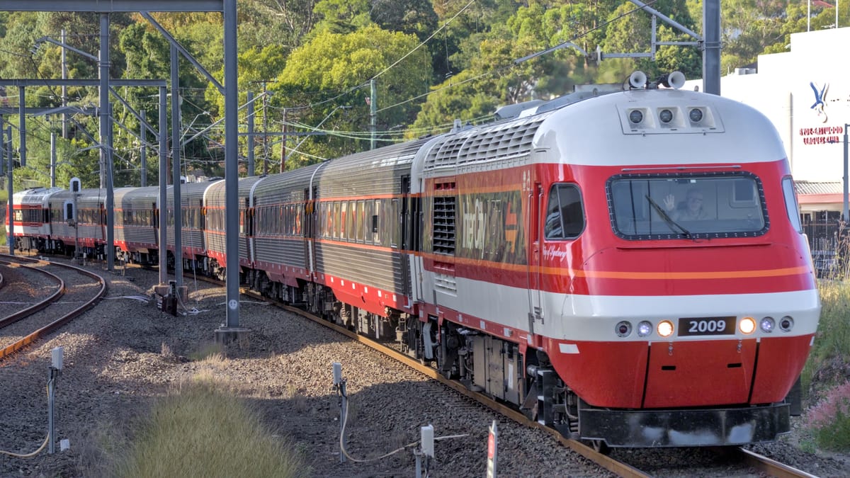 Distinctive red and white striped XPT power car leads six silver and black carriages around a slight curve
