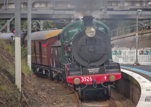 Head-on view of black and green steam locomotive rounding a tight curve next to a platform pushing vintage carriages