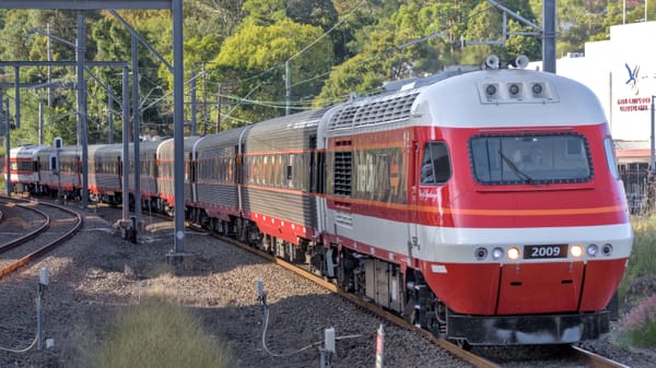 Distinctive red and white striped XPT power car leads six silver and black carriages around a slight curve